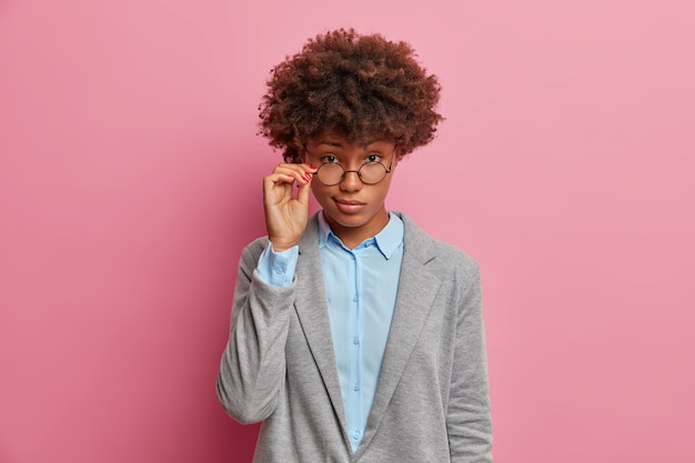 Self confident serious female director looks through glasses, dressed in formal clothes