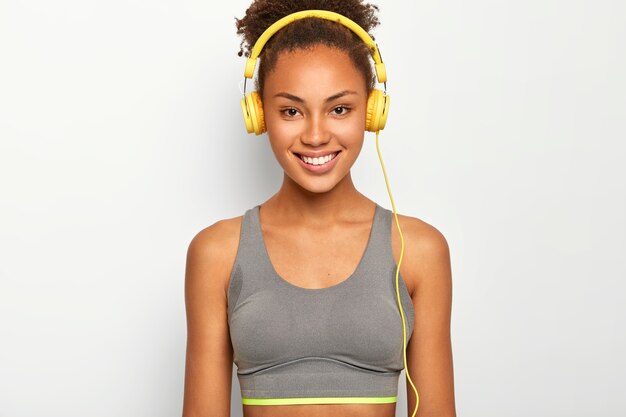 Self determined curly sportswoman chooses playlist for cardio workout, smiles pleasantly, wears casual top