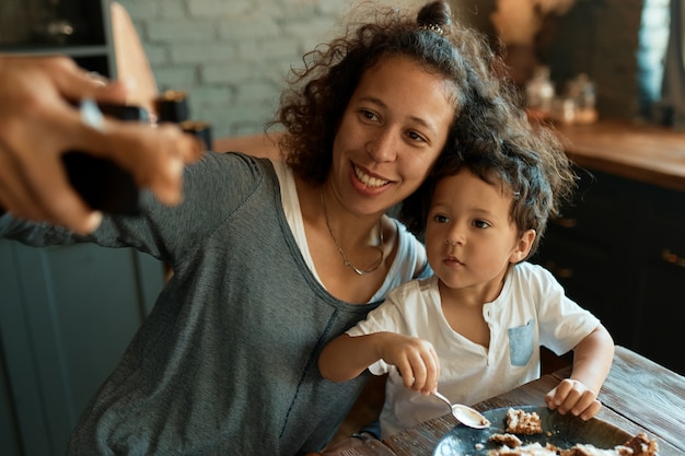 Self emloyed young woman having fun with her adorable baby boy holding smart phone