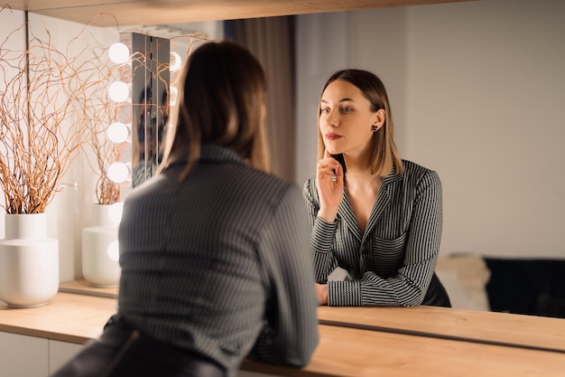 Бесплатное фото Уверенная в себе женщина смотрит на свое отражение в зеркале в помещении красивый дизайн интерьера