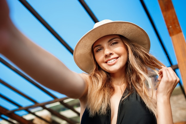 朝のビーチでかかっている帽子の美しい陽気な少女のSelfie