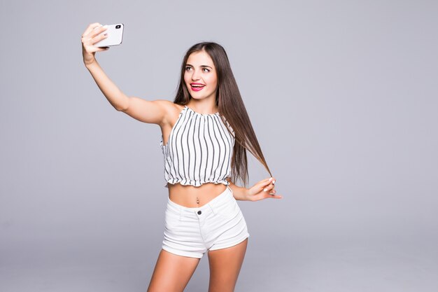 Selfie time. Joyful young women making selfie by her smart phone isolated on gray background