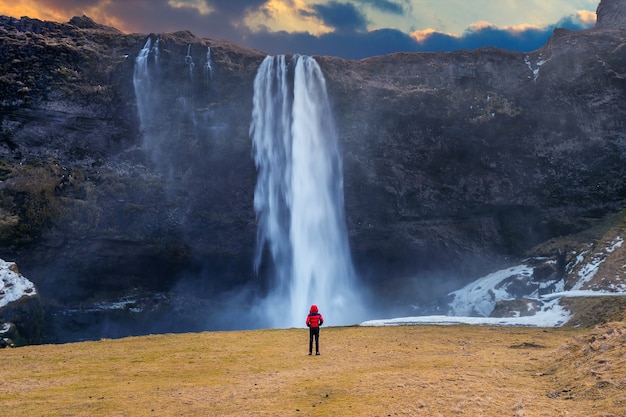 아이슬란드의 Seljalandsfoss 폭포. 빨간 재킷을 입은 남자가 셀야 란 즈 포스 폭포를 바라 봅니다.