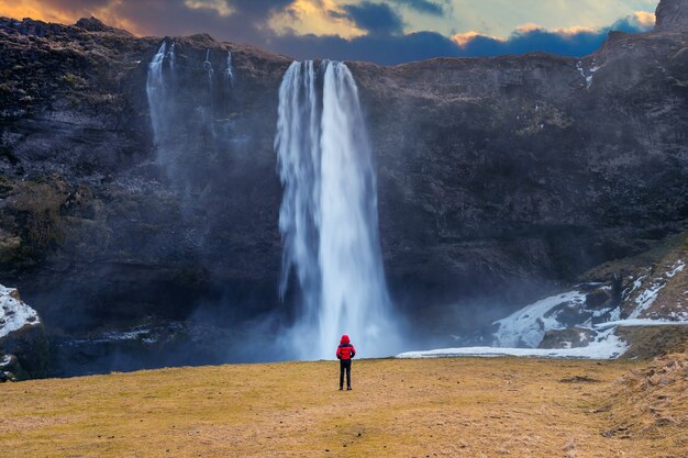 アイスランドのセリャラントスフォスの滝。赤いジャケットを着た男がセリャラントスフォスの滝を見ています。