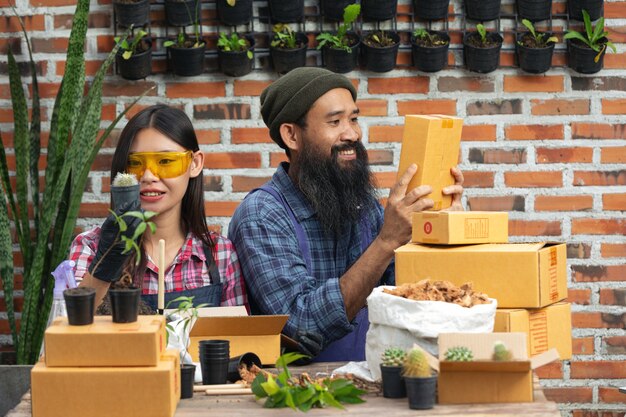 Selling plant online;sellers smiling and  holding pot of plant and shipping box in their hands