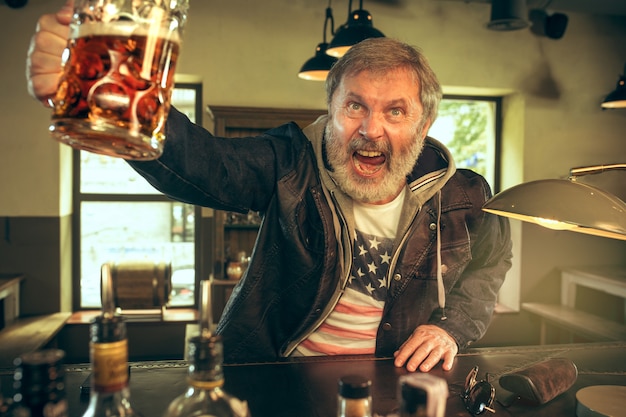 Free photo the senior bearded male drinking beer in pub