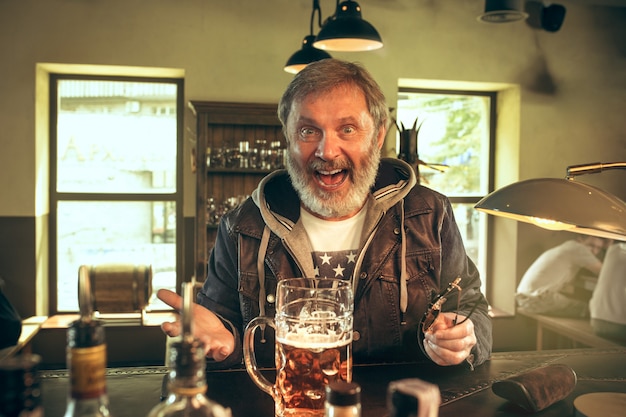 Free photo the senior bearded male drinking beer in pub