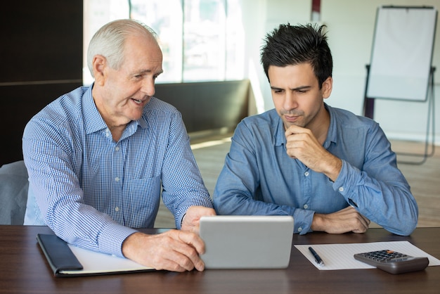 Free photo senior boss showing data to young employee on tablet