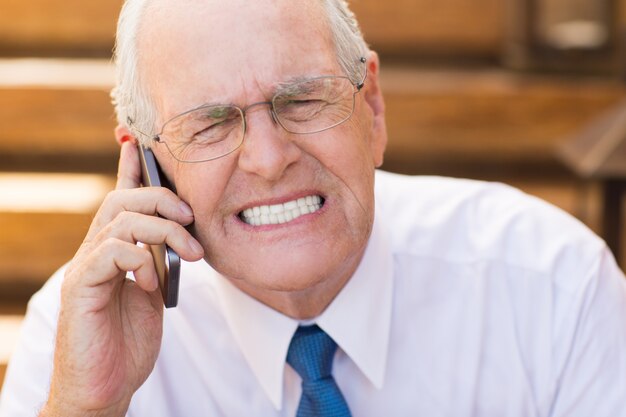 Senior business man clenching his teeth while talking on the phone