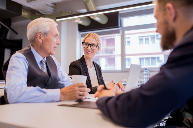 Senior businessman holding coffee cup sitting with his colleagues in the office