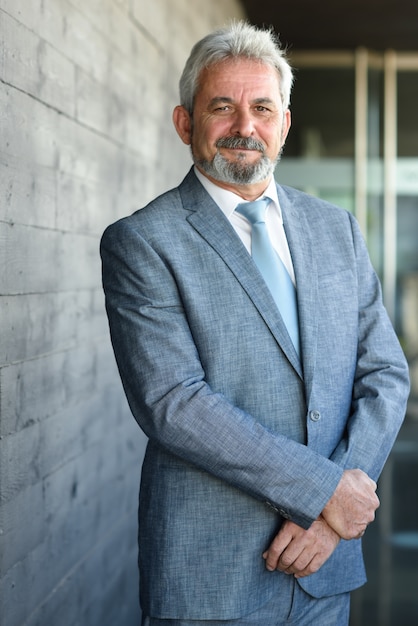 Senior businessman with arms crossed outside of modern office building.