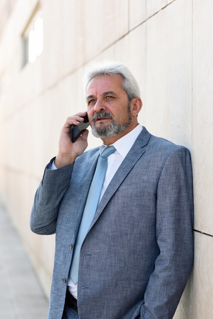 Foto gratuita uomo d'affari maggiore con smartphone al di fuori del moderno edificio per uffici.