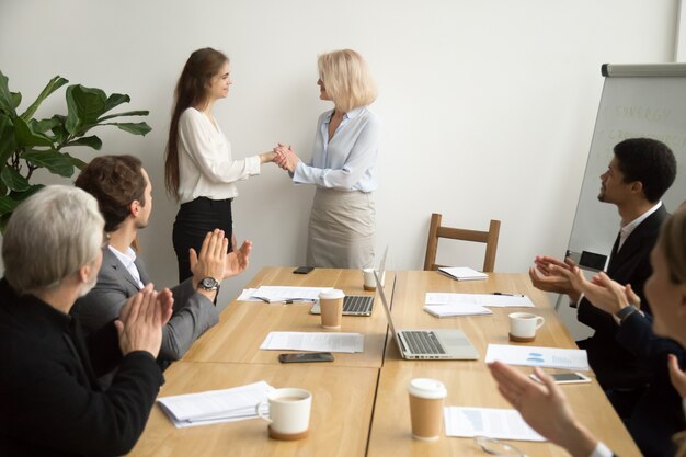 Senior businesswoman boss promoting thanking female employee while team applauding