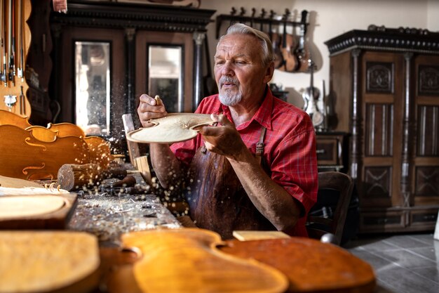 Старший плотник, работающий с твердой древесиной в мастерской и выдувающий опилки