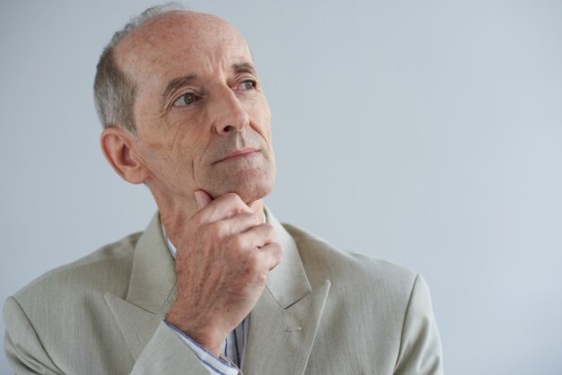 Senior Caucasian businessman touching chin and looking away with dreamy face