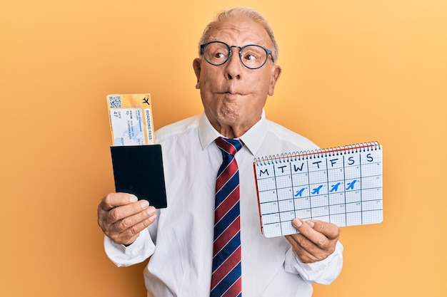 Free photo senior caucasian man going on business trip holding boarding pass making fish face with mouth and squinting eyes crazy and comical