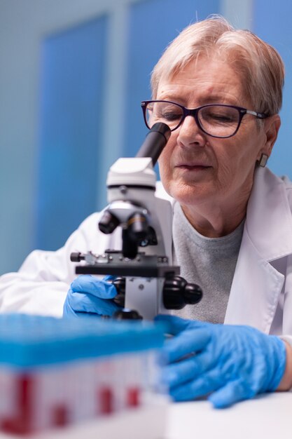 Senior chemist researcher in white coat looking in high end microscope for disease expertise