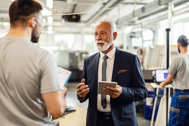 Senior company manager visiting employees in a factory plant and talking to one of the workers