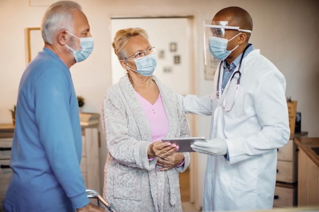 Free photo senior couple and black doctor wearing face masks while using touchpad at nursing home