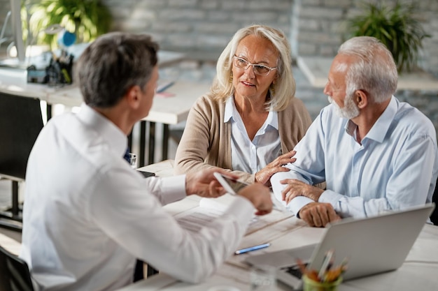 Senior couple communicating with insurance agent while having consultations with him in the office Focus is on woman