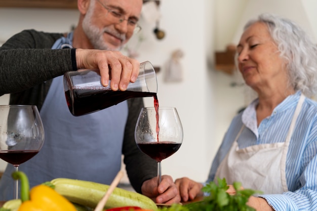 Foto gratuita coppia anziana che cucina insieme in cucina e beve vino