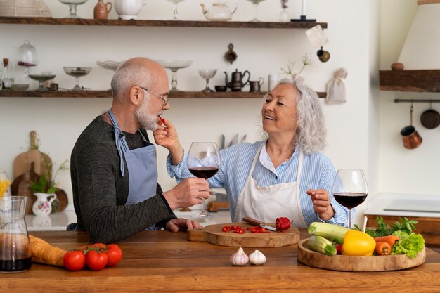 Пожилая пара готовит вместе на кухне и пьет вино