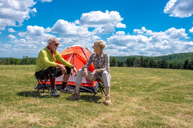 Senior couple having a rest in the field with a tent