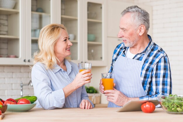 キッチンでお互いを見てジュースのガラスを保持している年配のカップル