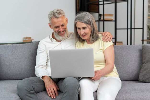 Senior couple at home on the couch using laptop