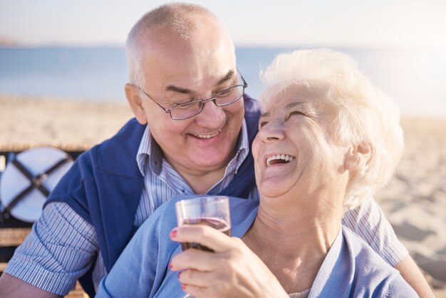 Senior couple hugging on the beach and drinking red wine