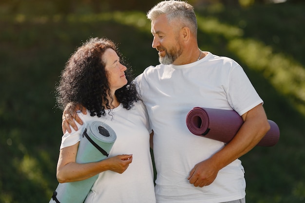 Free photo senior couple is doing yoga outdoors. stretching in park during sunrise. brunette in a white t-shirt.