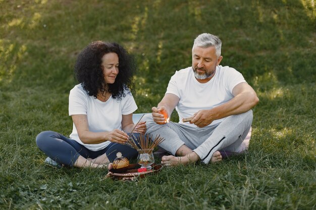 Senior couple is doing yoga outdoors. Stretching in park during sunrise. Brunette in a white t-shirt.