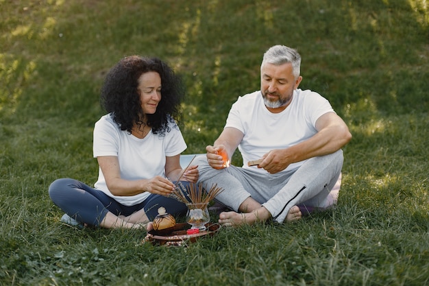 Senior couple is doing yoga outdoors. Stretching in park during sunrise. Brunette in a white t-shirt.