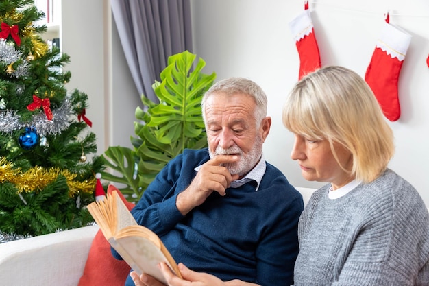 크리스마스 트리 장식을 배경으로 소파에 앉아 책을 읽는 노인 부부