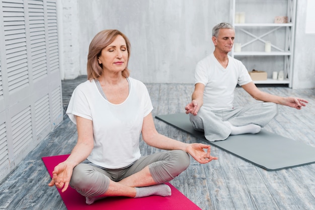 Senior couple performing meditation on exercise mat at home