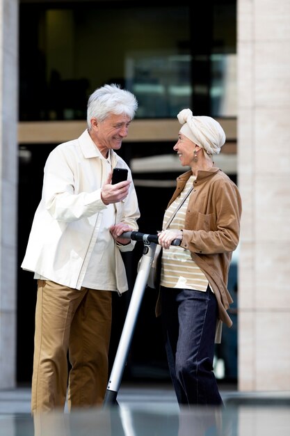 Senior couple riding an electric scooter in the city and using smartphone