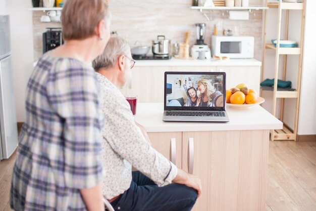 Senior couple talking with niece and daughter on online video call from kitchen. Elderly person using modern communication online internet web techonolgy.