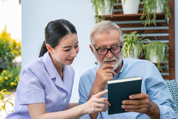 Senior elderly man reading book with nurse in garden