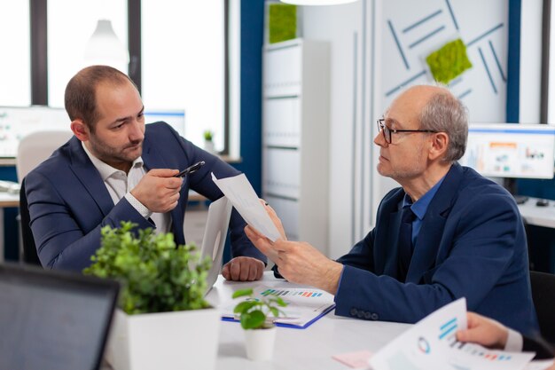 Senior entrepreneur discussing with coworker holding documents in conference during briefing Businessman discussing ideas with colleagues about financial strategy for new start up company