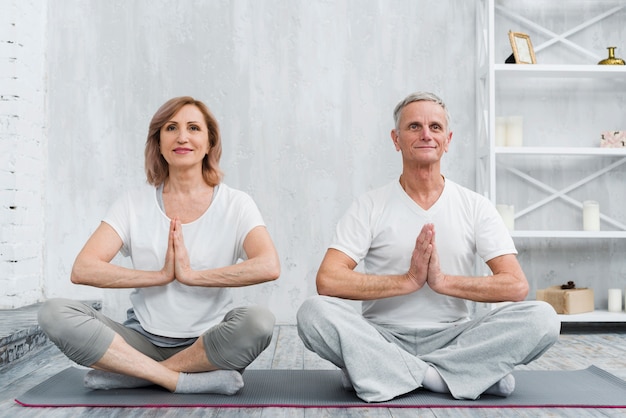 Foto gratuita le coppie senior della famiglia che si siedono nel loto posano sulla stuoia grigia di yoga