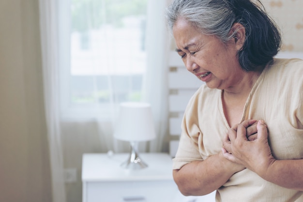 Asiatico femminile senior che soffre dal forte dolore nel suo attacco di cuore al petto a casa - malattia cardiaca senior