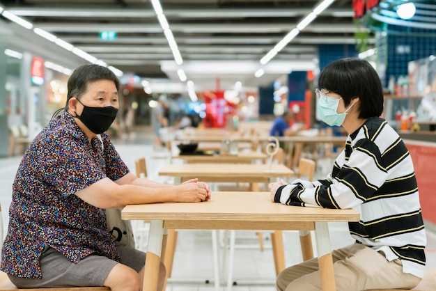 Una donna anziana e un giovane nipote si siedono a parlare a distanza con un nuovo stile di vita normale dopo il blocco dal virus corona covid19 diffuso nel grande magazzino del centro commerciale