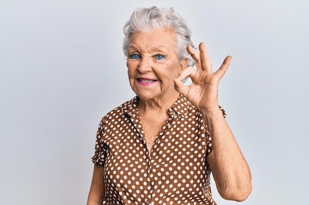 평상복을 입은 회색 머리 노인 여성은 손과 손가락으로 확인 표시를 하고 긍정적인 미소를 짓고 있습니다. 성공적인 표현