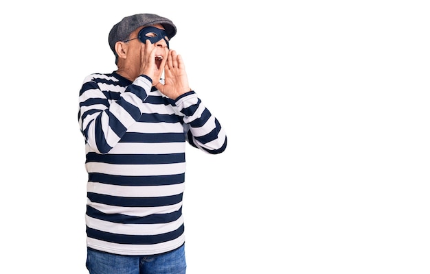 Free photo senior handsome man wearing burglar mask and t-shirt shouting angry out loud with hands over mouth