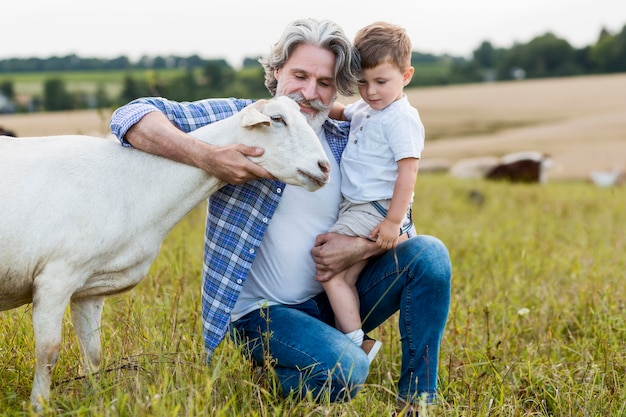 Foto gratuita senior holding ragazzino e abbracciando le capre