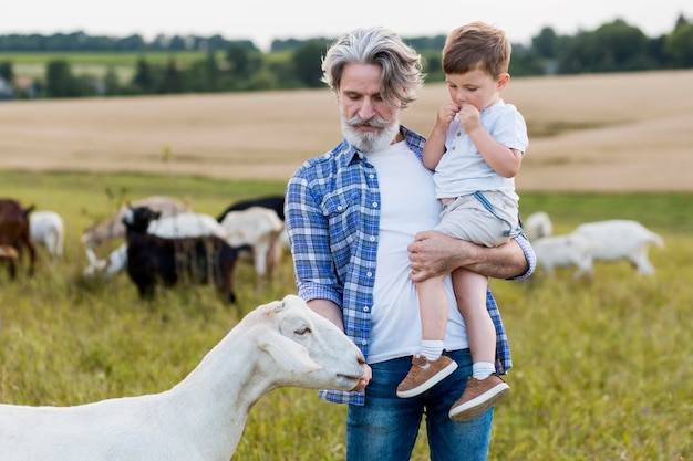 Старший держит маленького мальчика, играя с козами