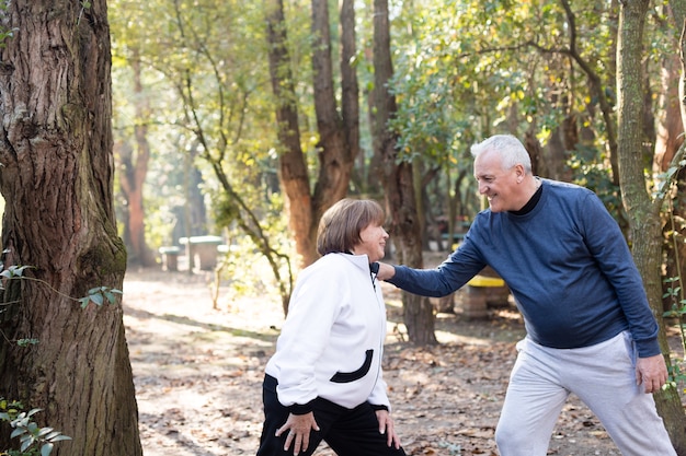 Senior husband stretching while touching his wife's shoulder