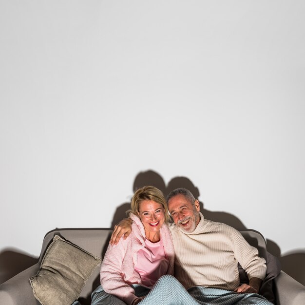 Senior laughing man hugging woman and watching TV on sofa