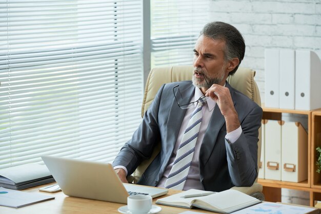 Senior lawyer thinking over the challenging legal case in his office biting eyewear temple