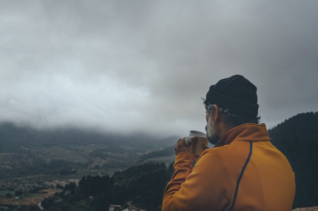 憂鬱な空の下でコーヒーを飲みながら景色を楽しむ年配の男性
